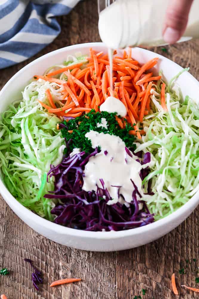 Pouring dressing on shredded and chopped veggies for vegan coleslaw. 