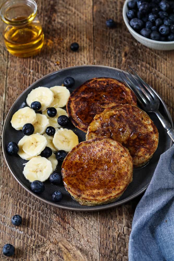 3 Vegan protein pancakes on a gray plate with banana coins and fresh blueberries on the side. 