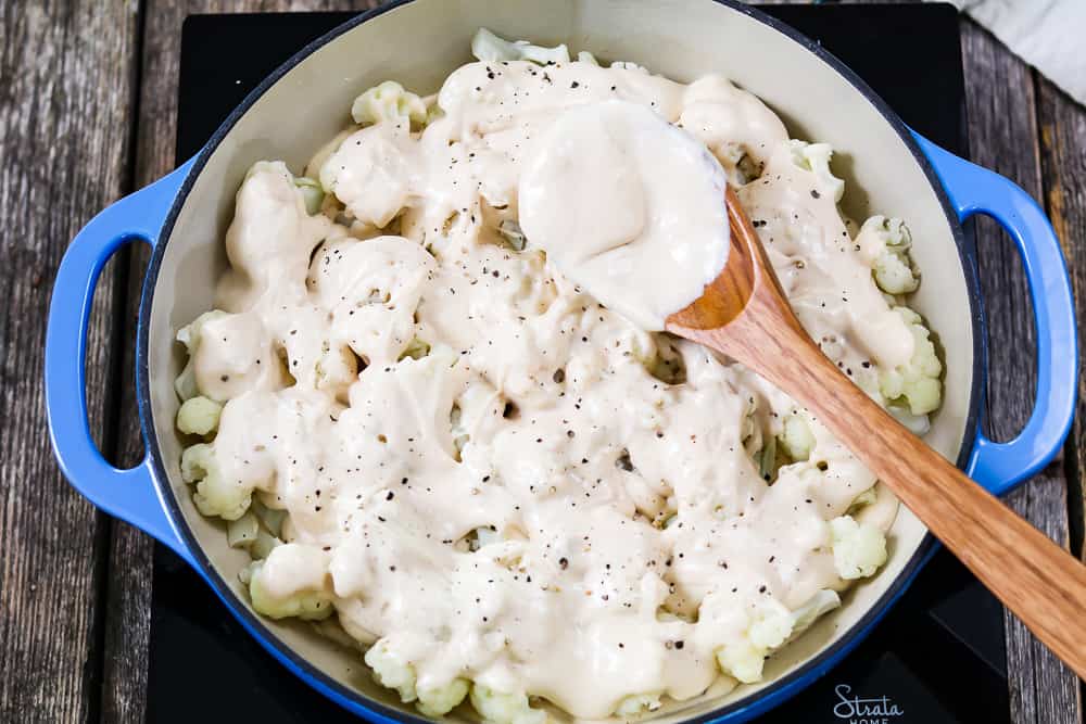 Topping cauliflower with vegan cheese sauce in a blue casserole dish. 