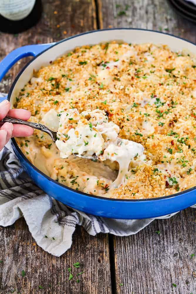 Vegan cauliflower casserole fully baked in a blue baking pan. Scooping out a cheesy portion. 