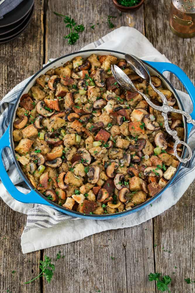 Vertical view of fully baked Vegan Sourdough Bread Stuffing in a blue casserole baking dish. Black serving plates on the side. 