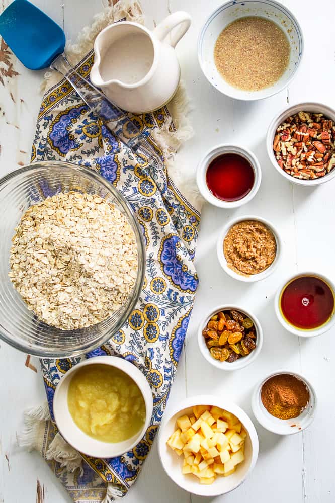 Ingredients for baked oatmeal muffins spread out of a white table in individual bowls. 