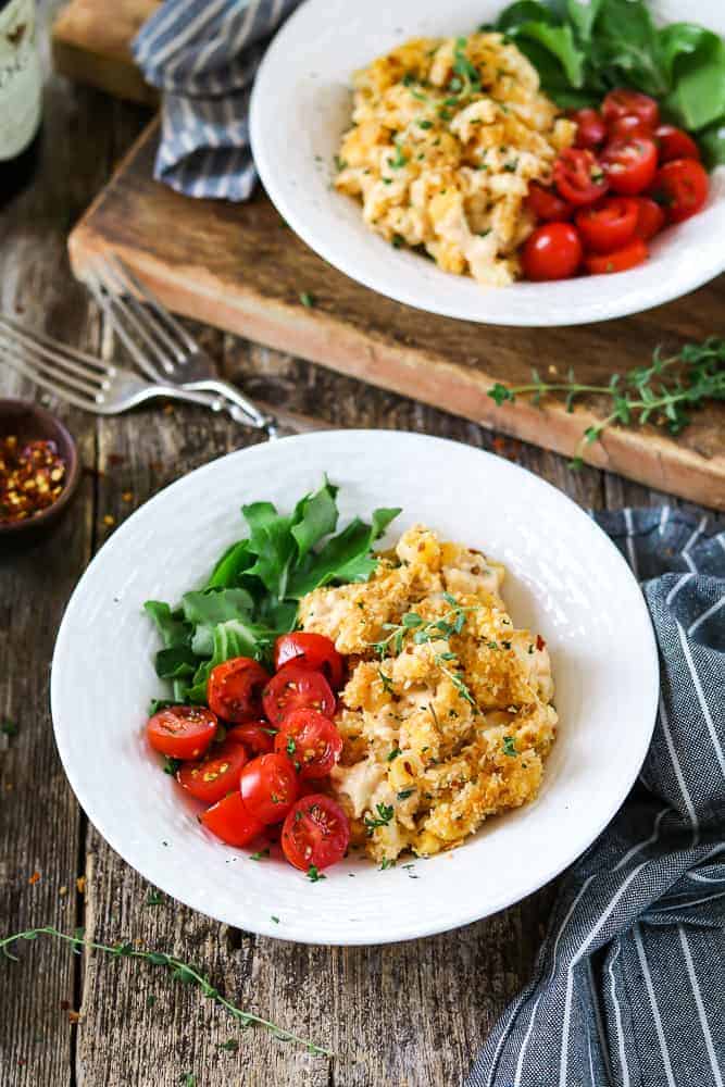 Two white bowls filled with baked vegan mac and cheese. Striped napkins and forks on the side. 