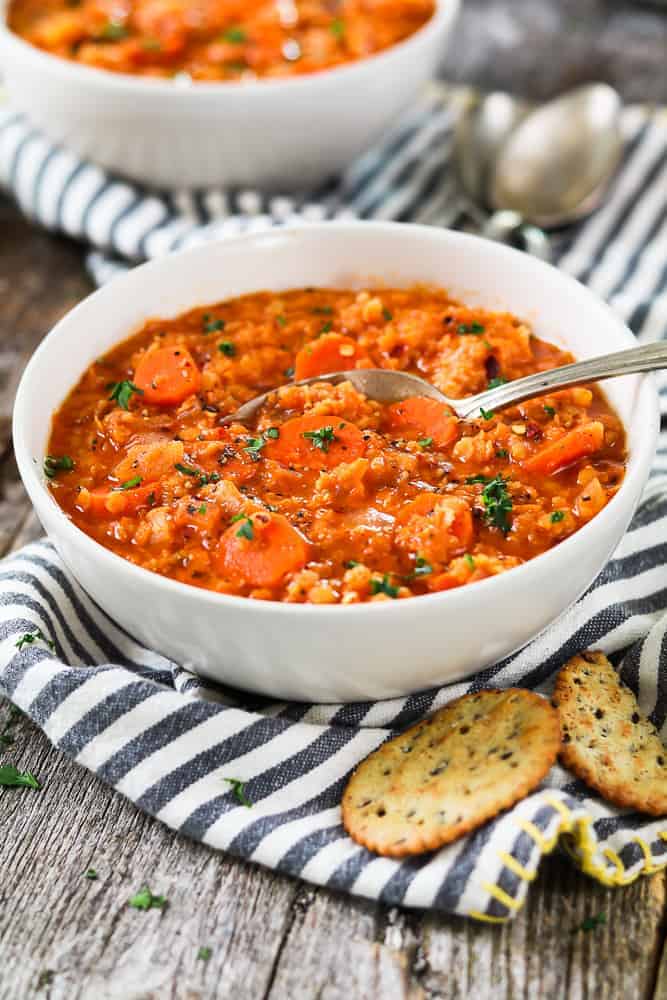 2 white bowls filled with red lentil soup and topped with fresh parsley. Two crackers on the side. 