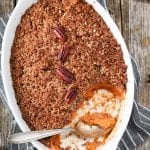 Overhead view of sweet potato casserole in a white serving dish. Small plates on the side.