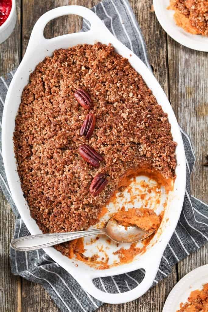 Overhead view of sweet potato casserole in a white serving dish. Small plates on the side.