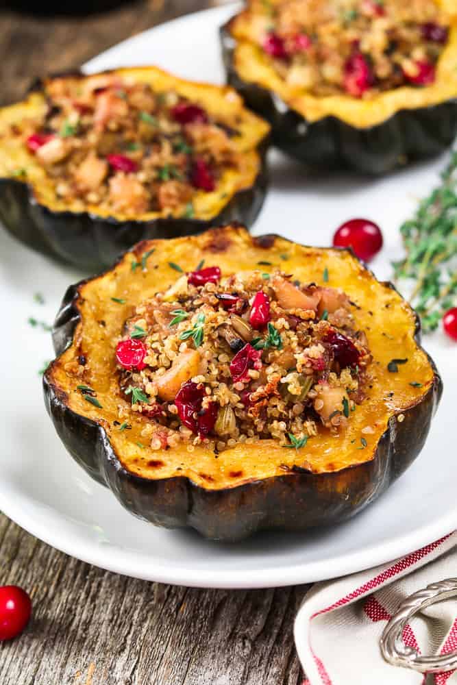 Three pieces of stuffed acorn squash on a white serving platter. Fresh cranberries and thyme on the side.