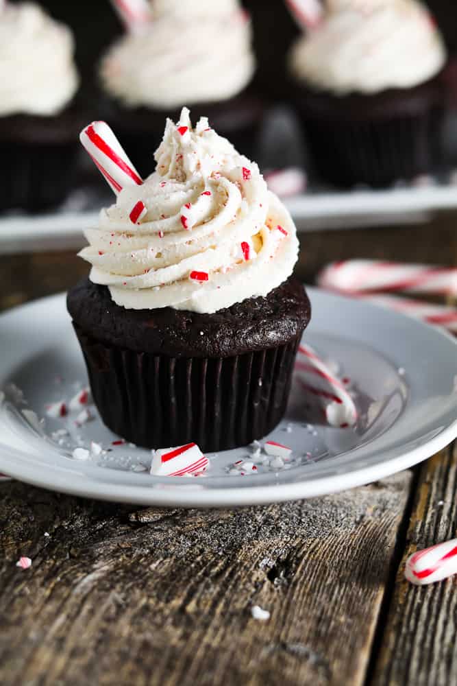 close up photo of chocolate peppermint cupcakes on a white plate. Crushed candy canes on the plate. 