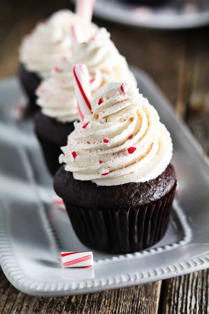 3 cupcakes in a row on a white platter. Candy cane pieces on the side. 