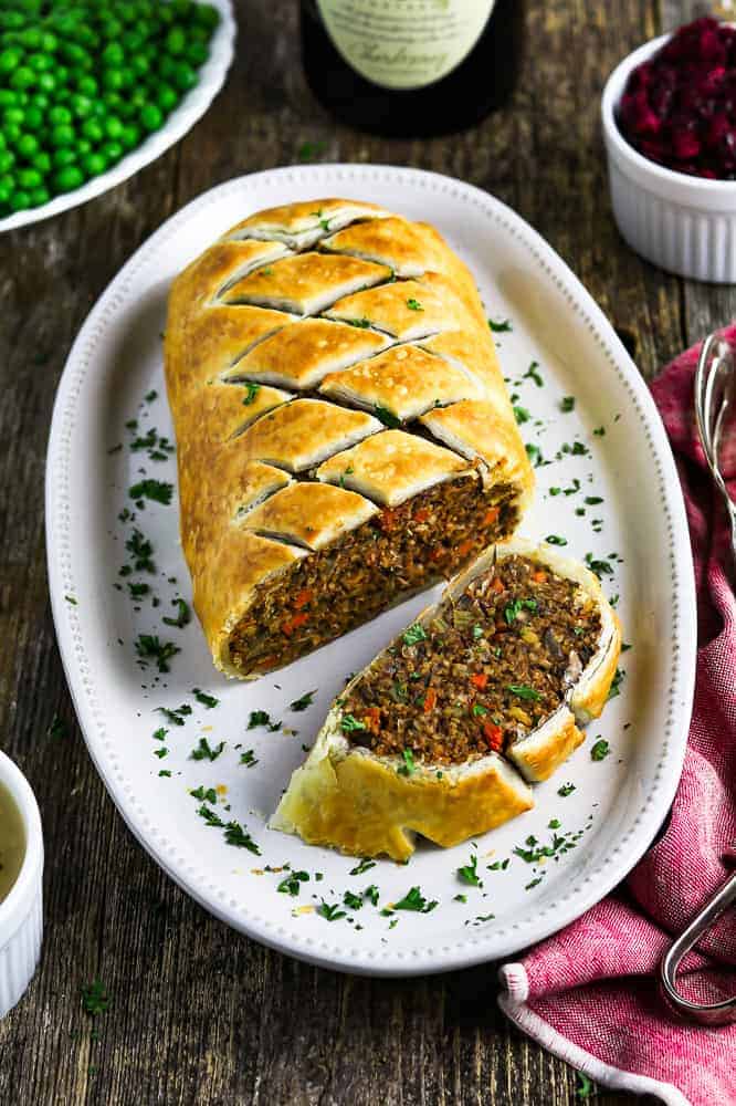 vegan wellington cut into slices on a white platter. Peas and cranberry sauce on the side.