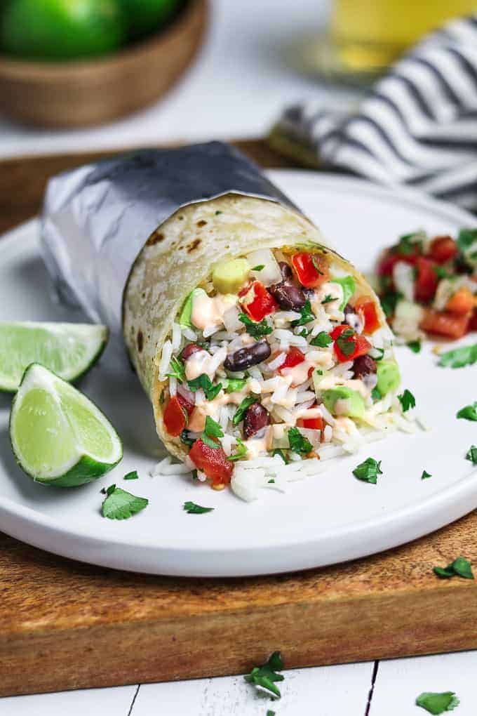 front view of vegan burrito on a white plate. Lime and pico del gallo on the side. 