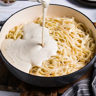 pouring alfredo sauce on top of pasta.