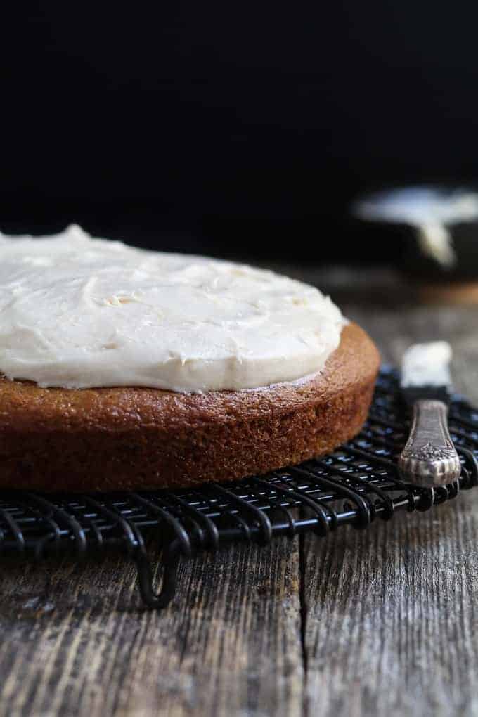 front view of vanilla cake topped with vegan cream cheese frosting. Bowl of frosting in the background.