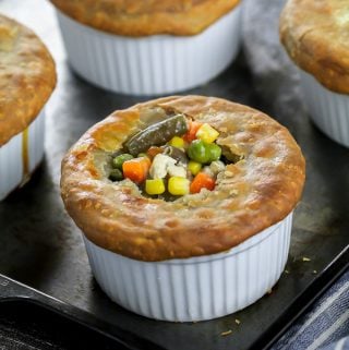 four fully baked vegan pot pies in a ramekin. Closeup shot of one vegan pot pie with veggies popping out the top.