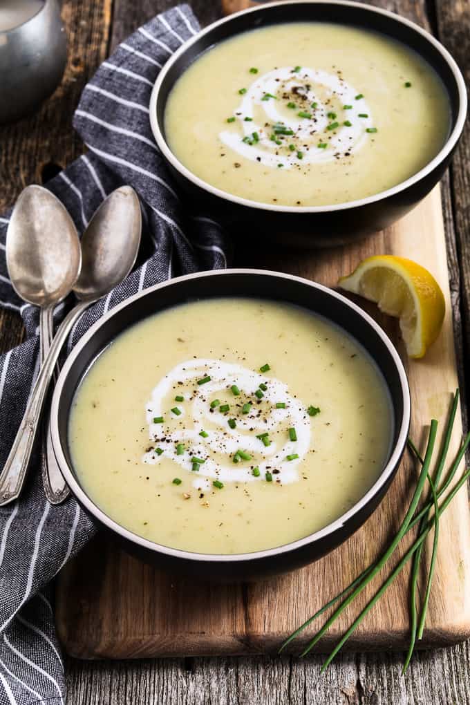 Two black bowls filled with Instant Pot Potato Leek Soup and topped with coconut milk and chives. Striped napkins and spoons on the side. 