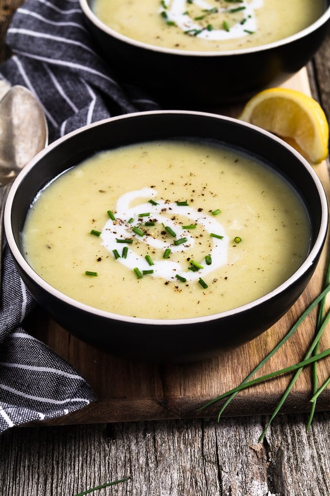 two black bowls of instant pot potato leek soup topped with coconut cream and chives. 