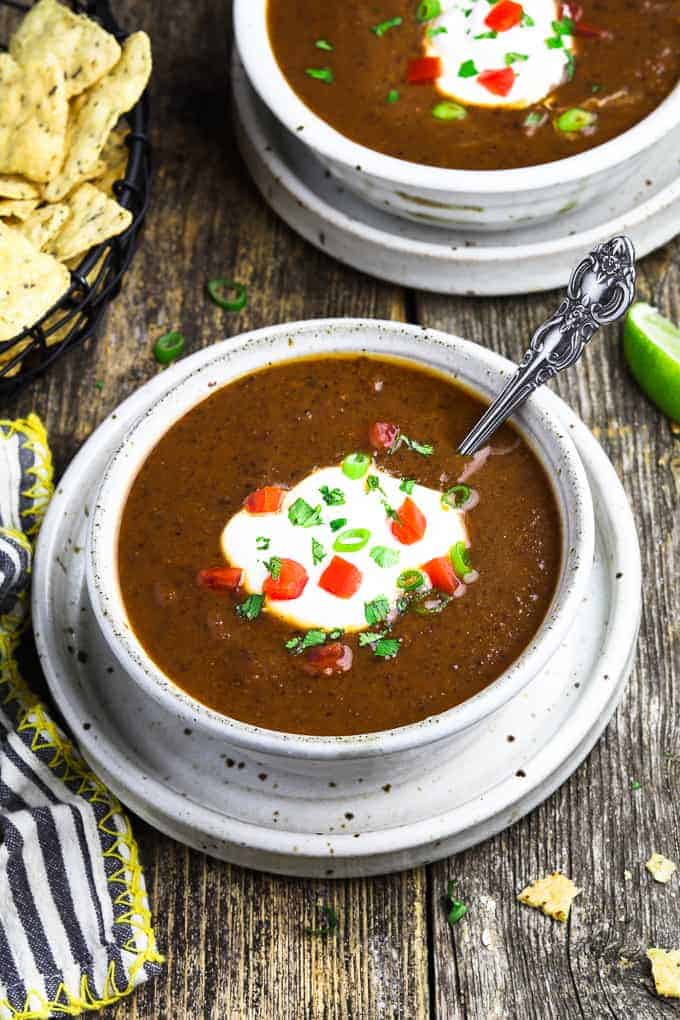 two white bowls filled with Mexican black bean soup and tortilla chips on the side. 