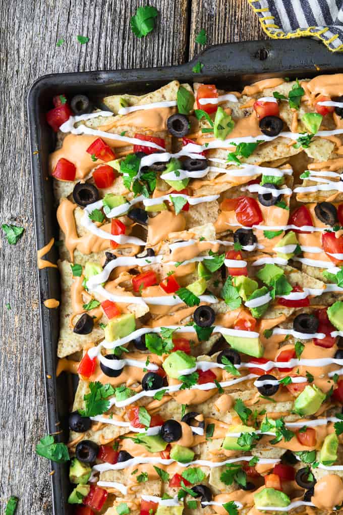 overhead view of vegan nachos in a baking pan and loaded with toppings. 