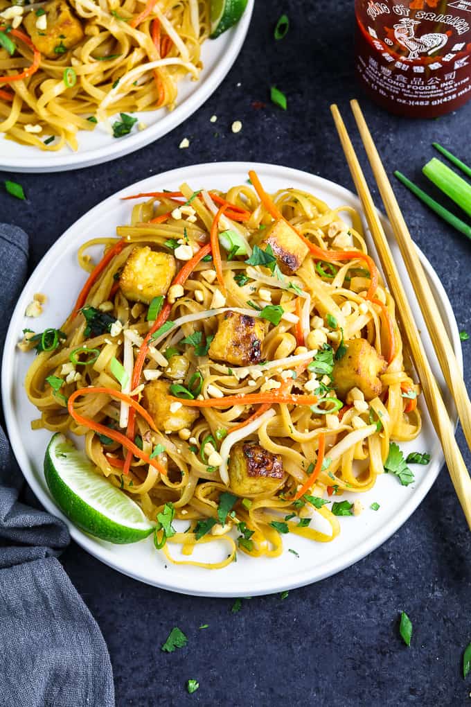 Overhead view of two white plates topped with vegan pad Thai with chop sticks and sriracha on the side. 