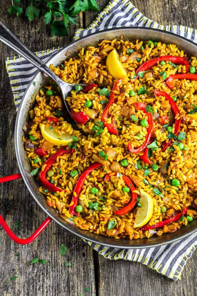 overhead view of fully cooked vegan paella in a pan. Lemon wedges on top.