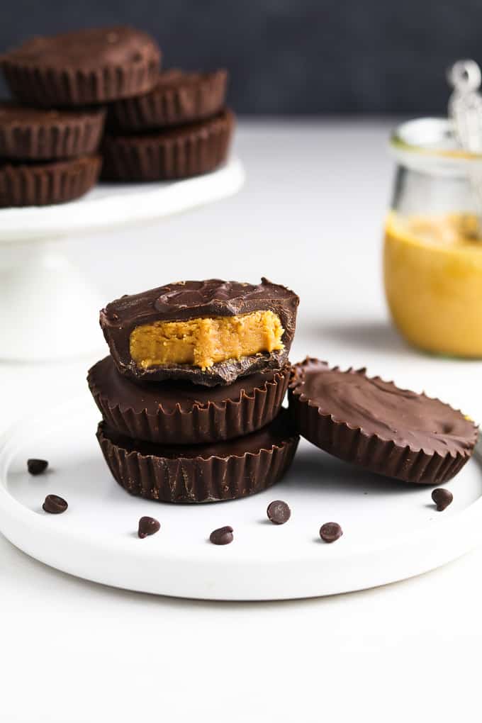 three peanut butter cups on a white plate. Peanut butter in the background. 