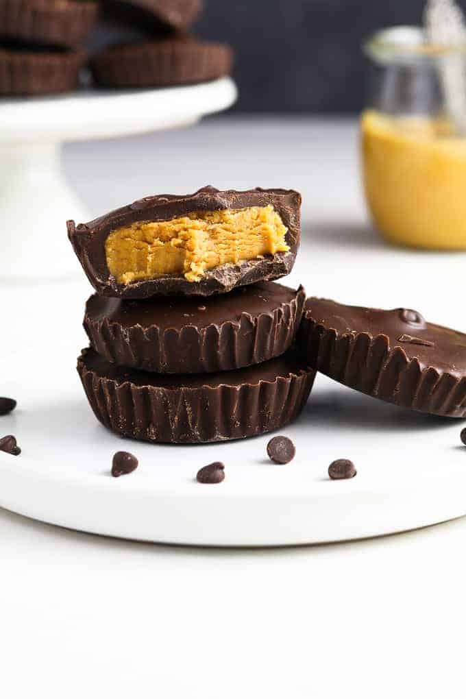 close up view of three vegan peanut butter cups on a white plate with peanut butter in the background. 