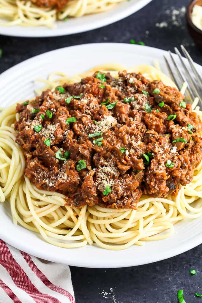 Close up view of vegan bolognese on top of spaghetti on a white plate with fork on the side. 