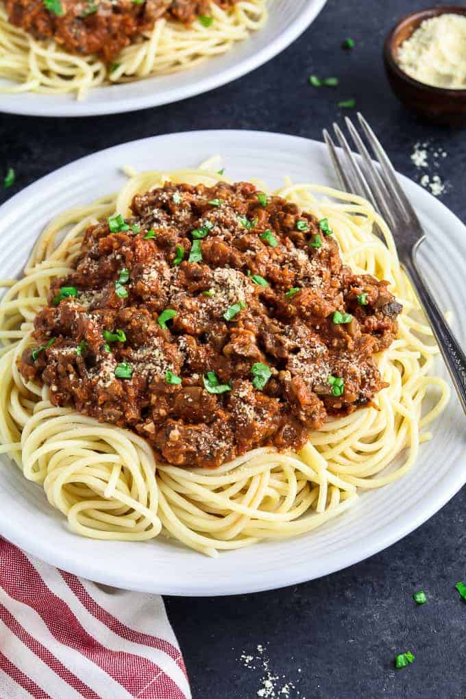 White plate topped with pasta and vegan bolognese sauce. Vegan parmesan on the side.