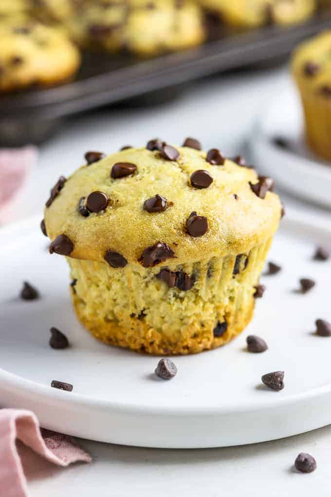 close up photo of vegan chocolate chip muffin on a white plate with more muffins in the background. 