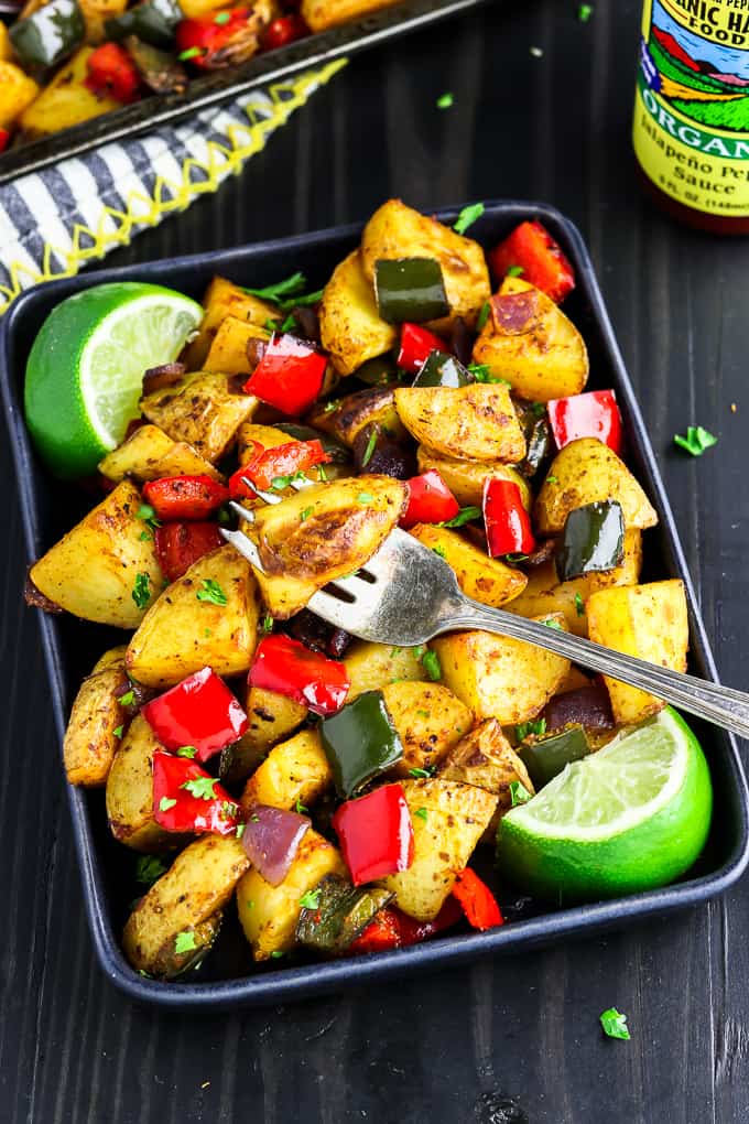 Black plate filled with roasted breakfast potatoes with lime wedges on the side. 