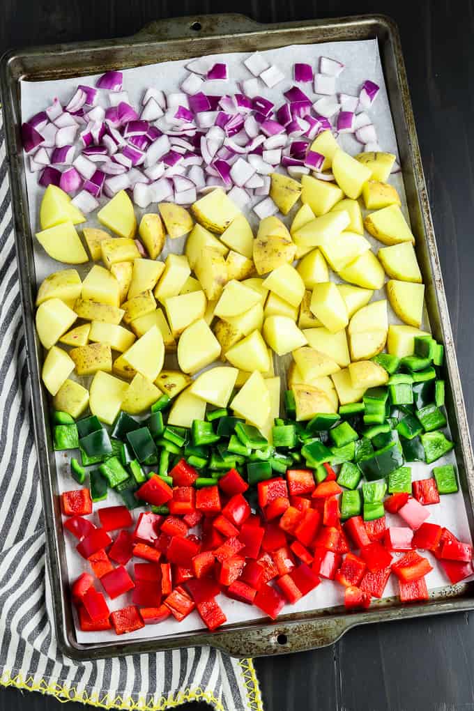 Process photo of a baking sheet filled with cut onions, peppers and potatoes. 