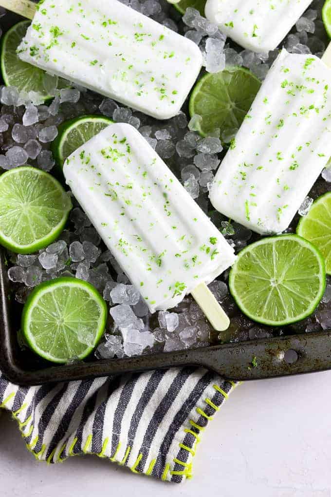 4 coconut lime popsicles on a baking tray with ice and lime slices. 