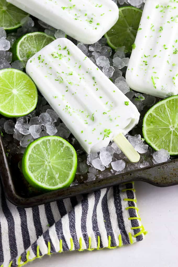 Closeup view of a popsicle on a baking tray with limes and ice on the bottom. 