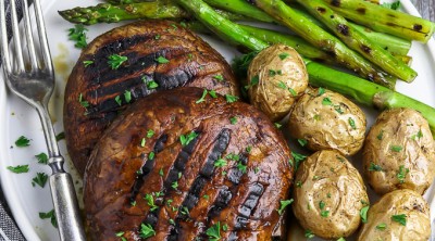 overhead view of two portobello mushroom steaks on a white plate. Asparagus and potatoes on the side.
