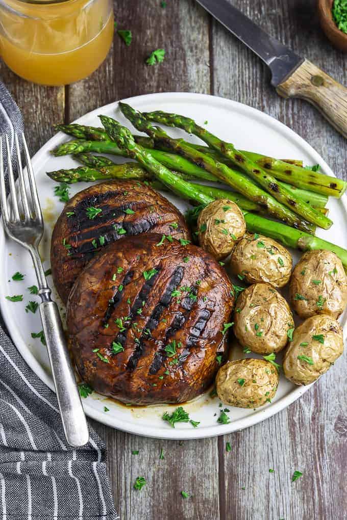 overhead view of two portobello mushroom steaks on a white plate. Asparagus and potatoes on the side.