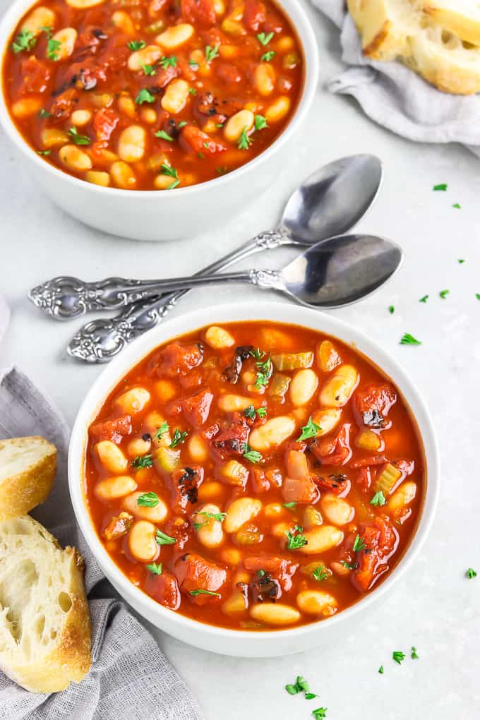Two bowls of tomato white bean soup topped with parsley and spoons in the middle. 