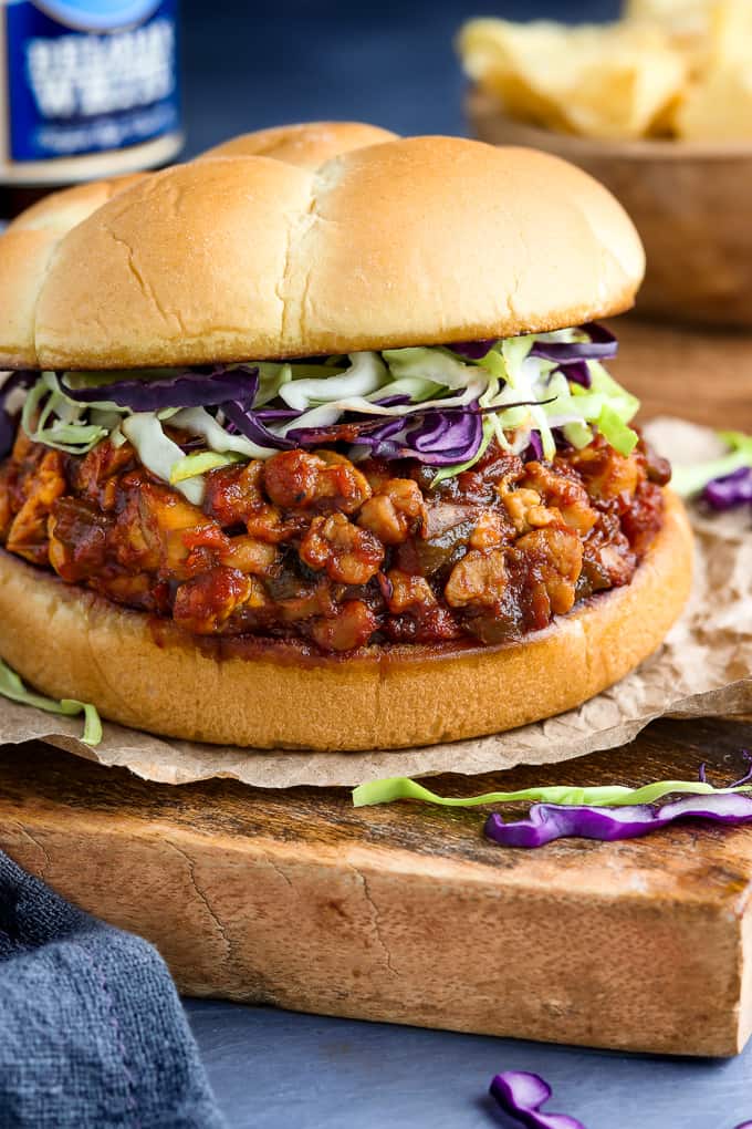 Side view of assembled vegan sloppy joes with chips and beverage in the background.