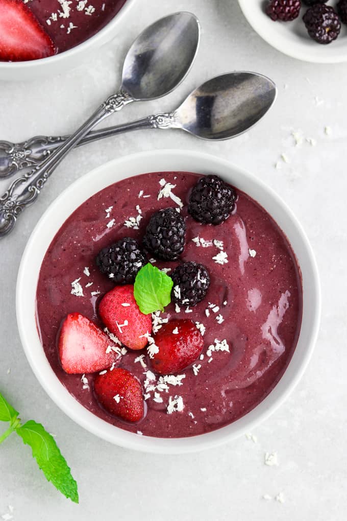 Overhead view of acai bowl topped with fruit and mint sprig. Spoons on the side. 