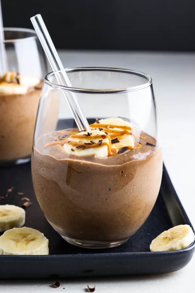 Front view of two smoothies topped with banana slices and peanut butter swirl. 