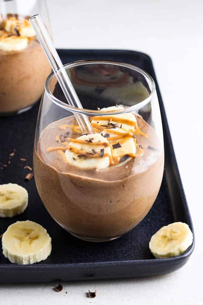 Chunky monkey smoothie in a glass on a black tray with banana slices on the side. 