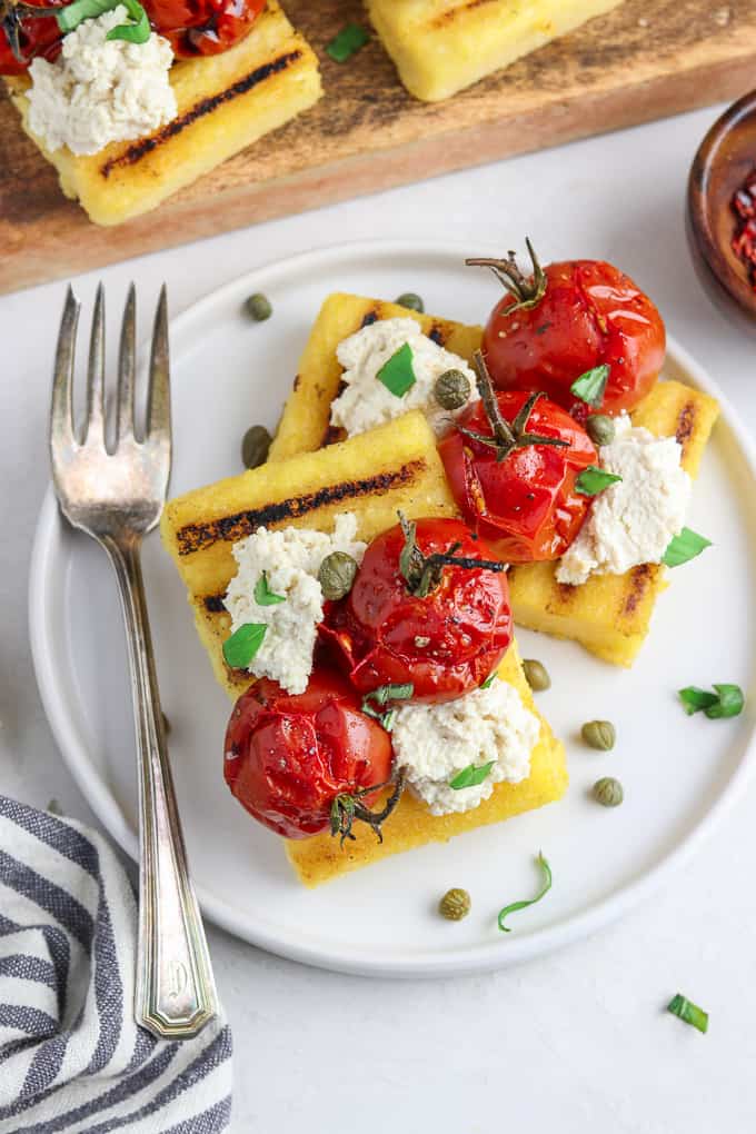 Overhead view of grilled polenta on a white plate with fork and napkin on the side. 