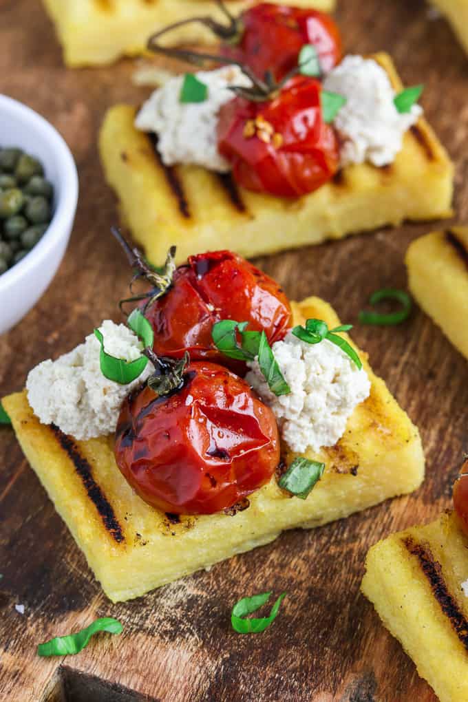 Grilled polenta on a cutting board with capers on the side. 
