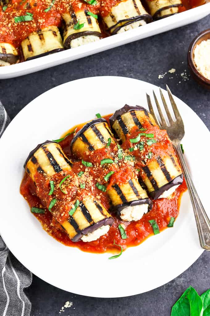 overhead view of 3 pieces of eggplant rollatini on a white dish with fork on the side. 
