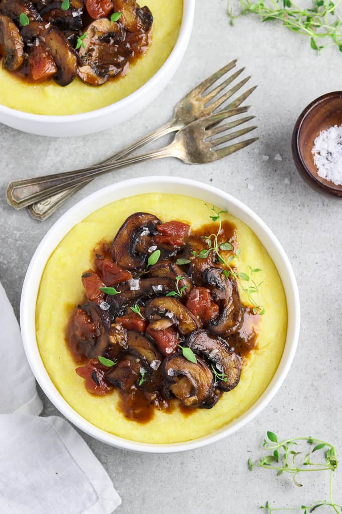 Overhead view of two bowls of creamy polenta on a table with forks in between. 