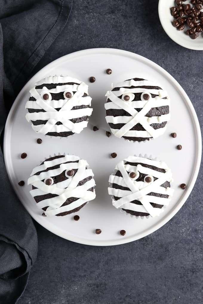 overhead view of 4 mummy cupcakes on a white plate with black napkin on the side. 