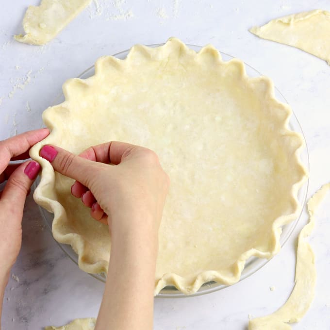 Fluting a pie crust with fingers. 