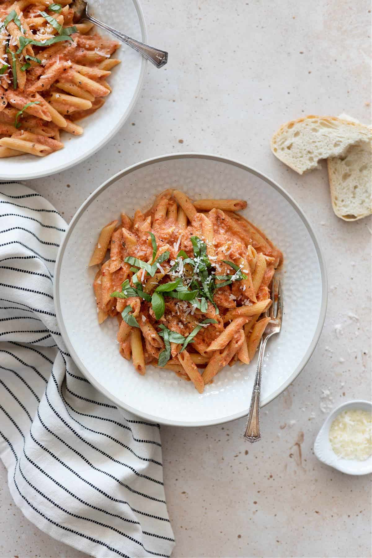 Overhead view of two bowls of vegan penne all vodka with bread on the side. 