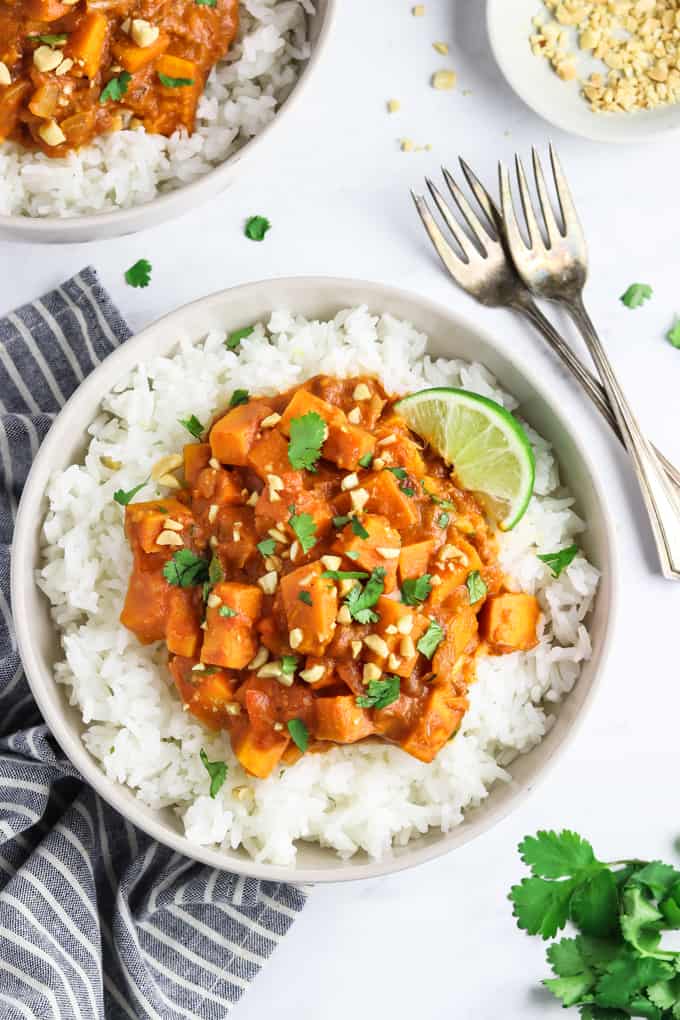  bovenaanzicht van twee kommen zoete aardappelcurry met een gestreept servet en vorkjes ernaast.