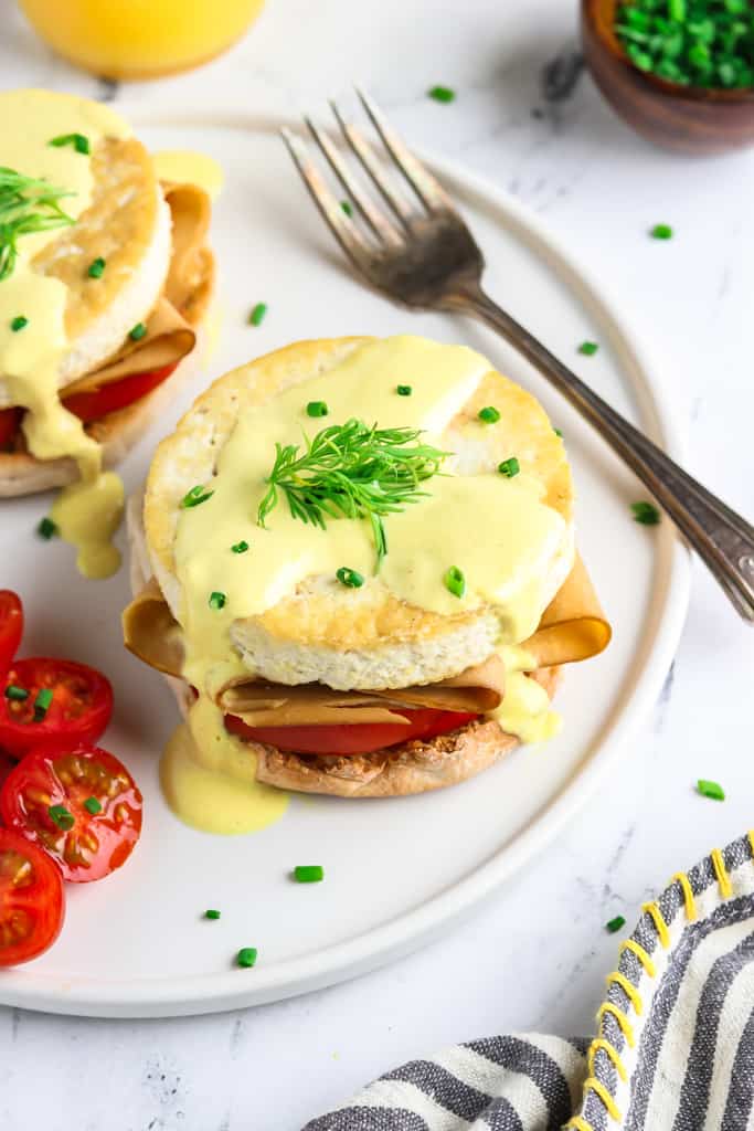 Vegan eggs benedict on a white plate with tomatoes and fork on the side. 