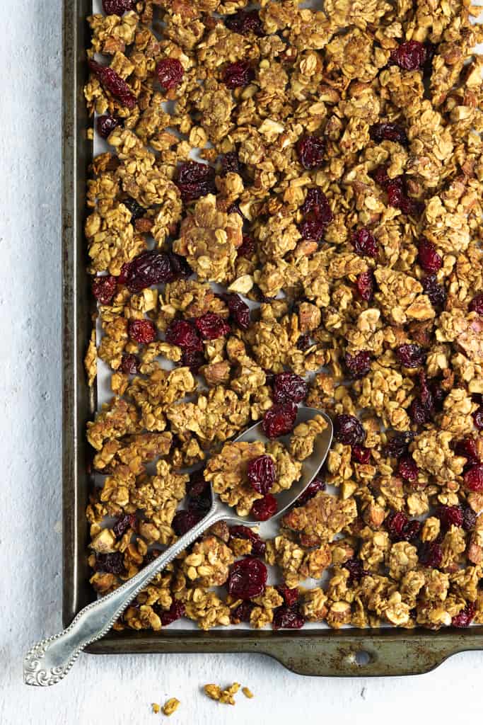 Overhead view of vegan granola on a baking sheet with a spoon on top. 